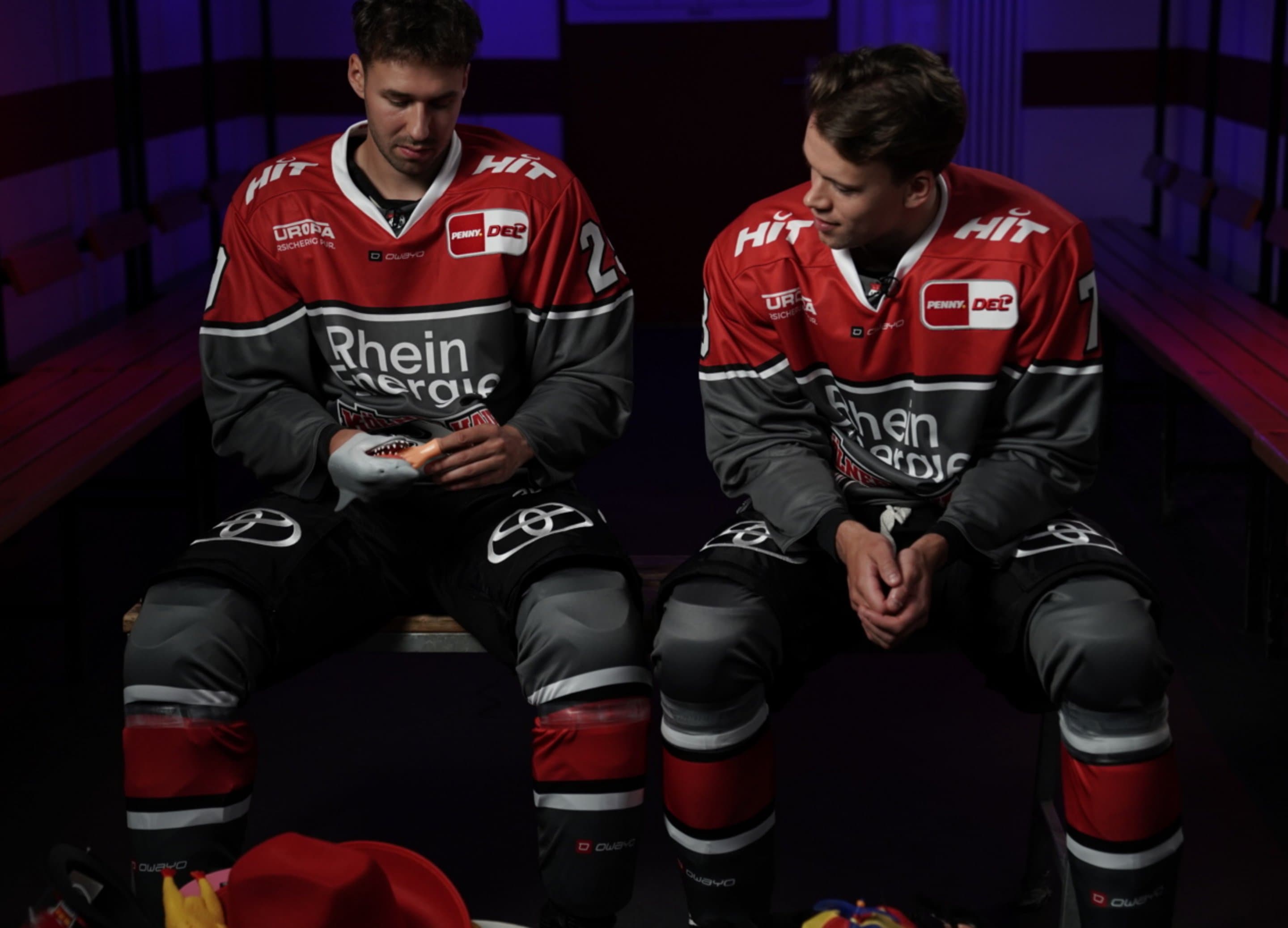 Zwei Spieler der Kölner Haie sitzen in der Umkleidekabine mit Karnevalsartikeln - Symbolbild für das Sponsoring der Kölner Haie durch NetCologne