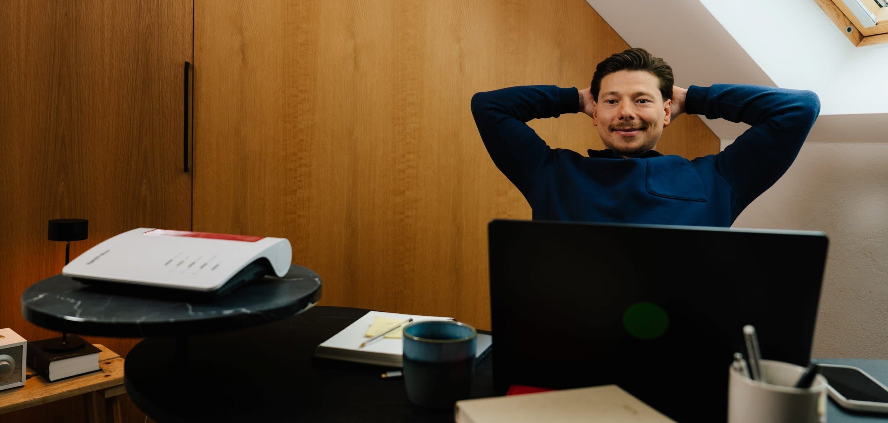 Person sitzt entspannt und zufrieden am Schreibtisch im Homeoffice vor einem Laptop - Sinnbild für stabiles Glasfaser-Internet im zuhause.