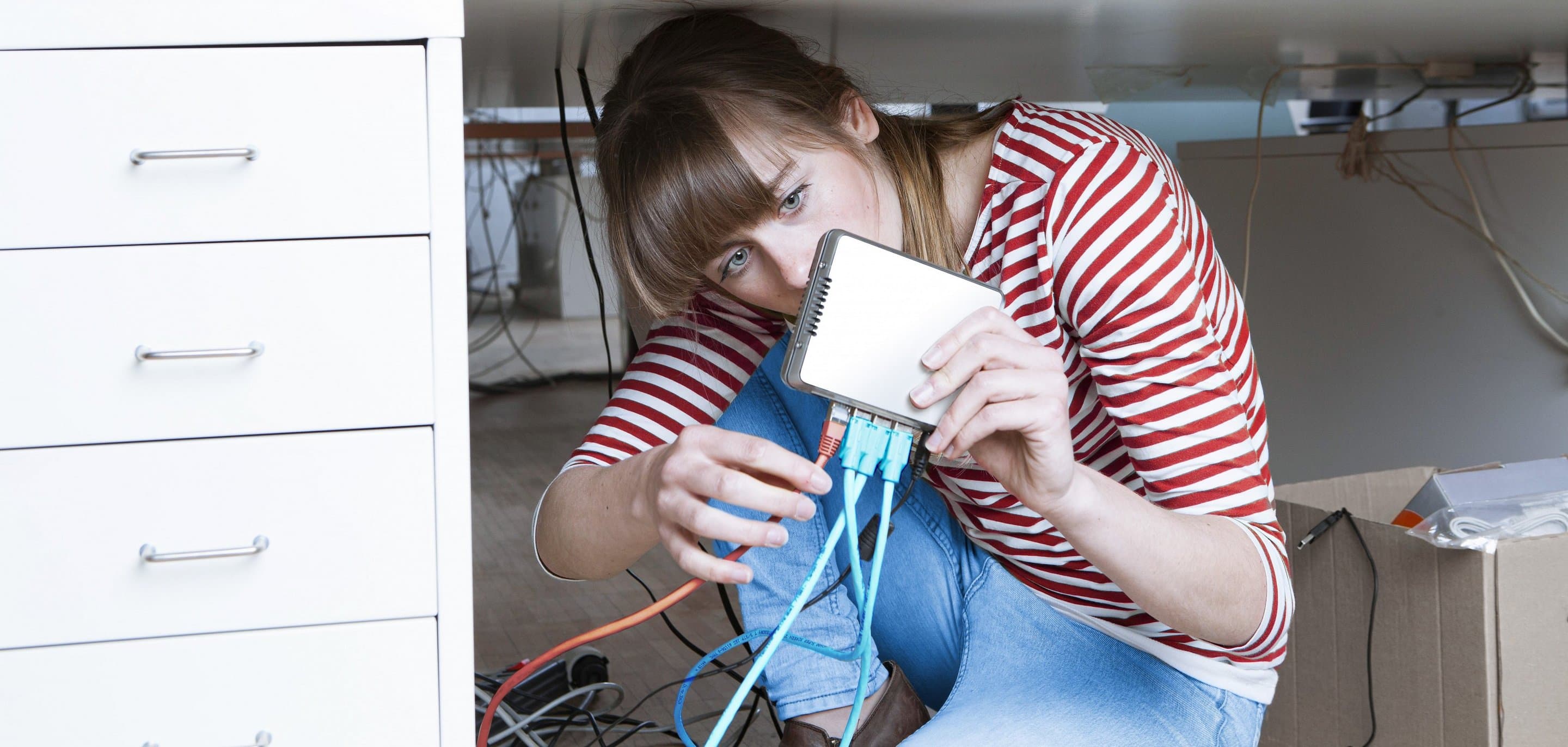 Frau sitzt unter Schreibtisch und steckt ein Kabel in einen Router