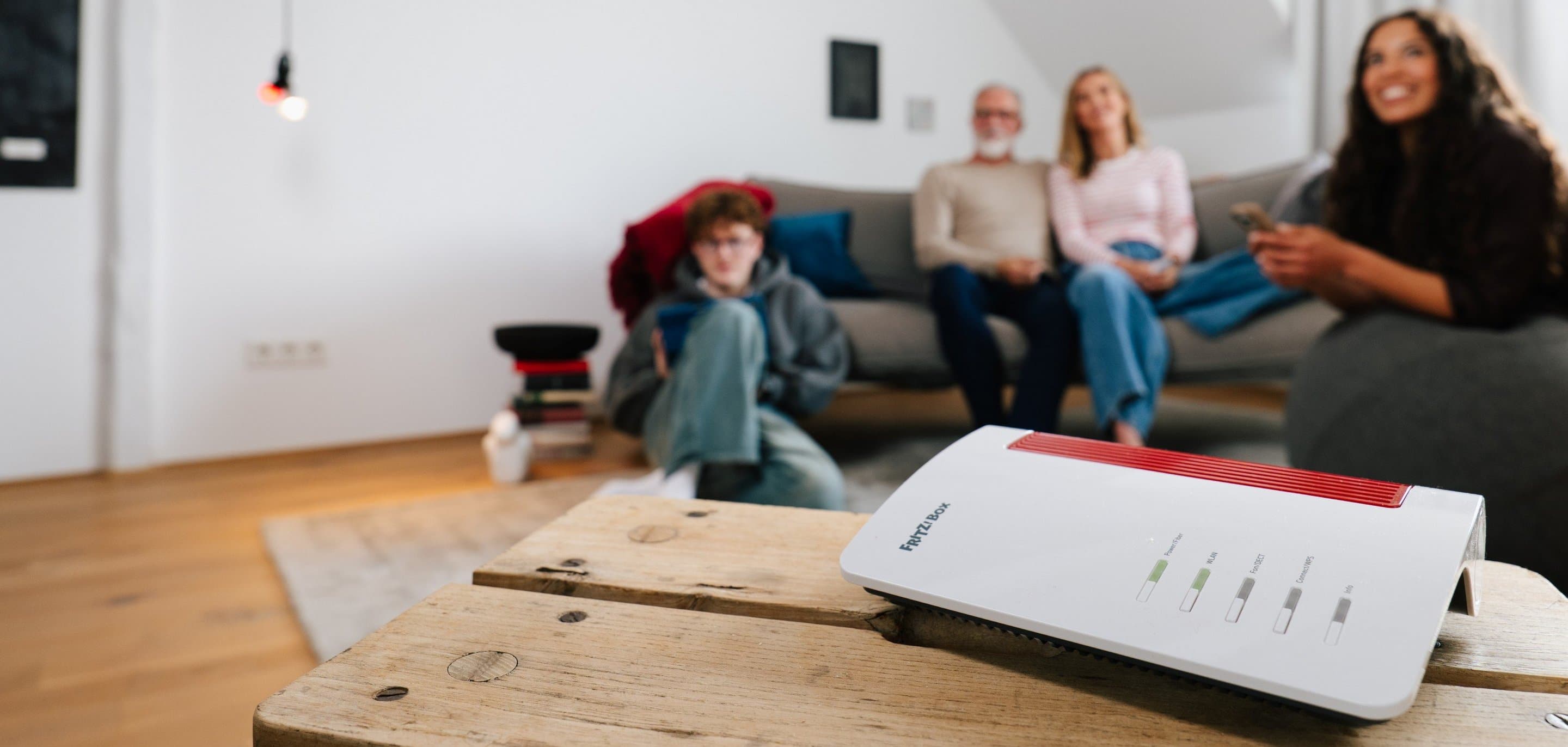 WLAN-Reichweite verbessern im Zuhause: Router auf dem Boden vor Sofa positioniert, während mehrere Personen im Wohnzimmer Smartphones und Tablets nutzen.