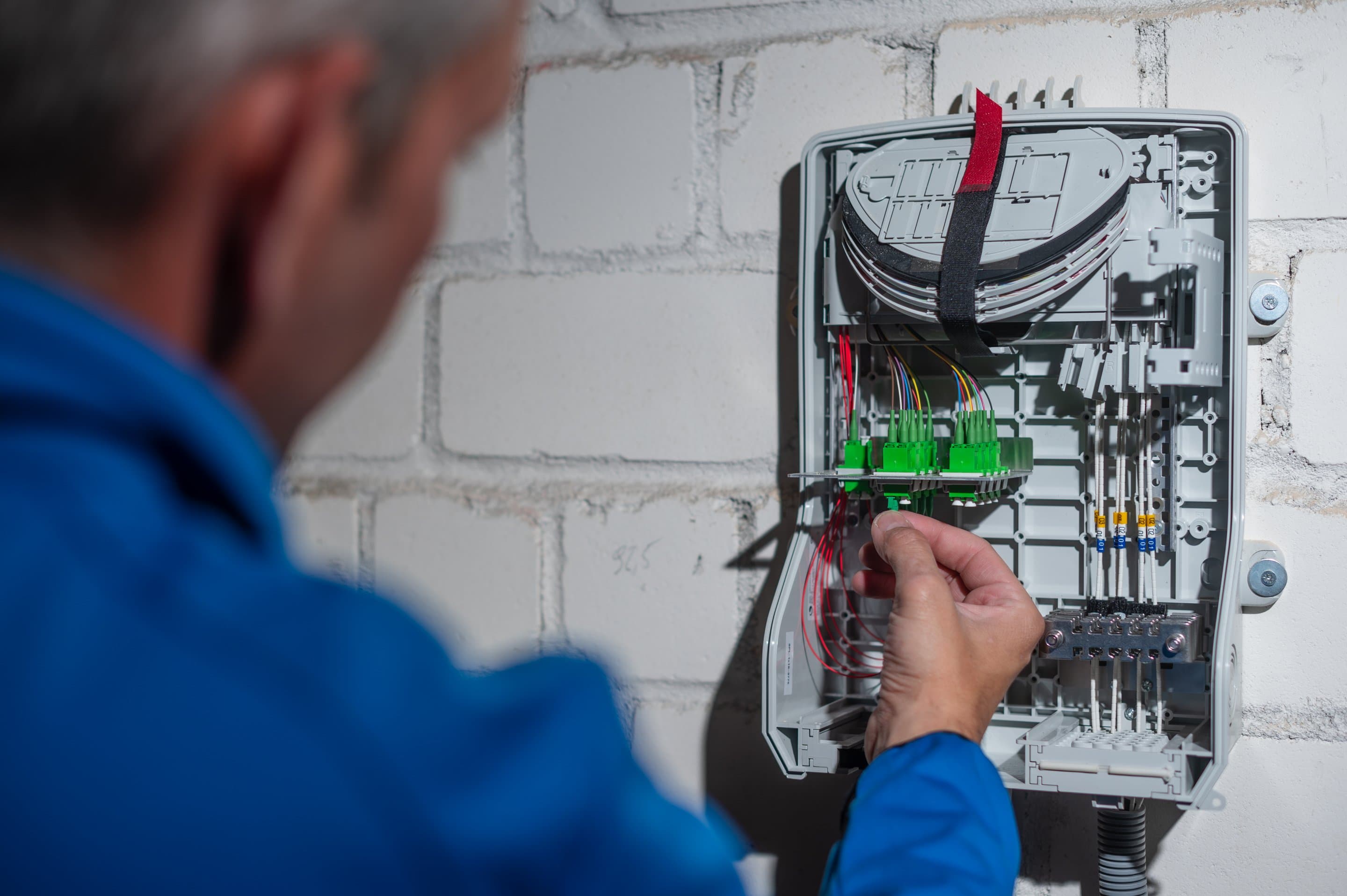 Herstellung des Glasfaserhausanschlusses NetCologne Techniker schließt die Glasfaserleitung an den Hausanschlusskasten an