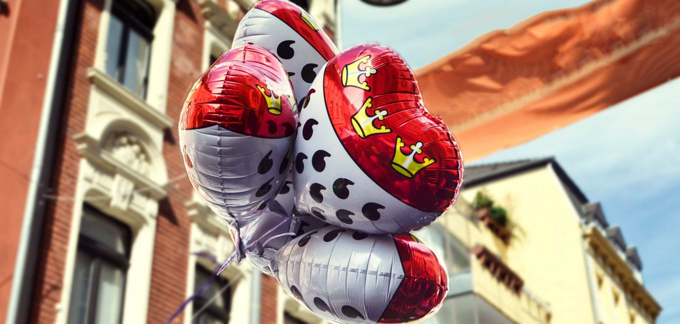 Luftballons mit dem Kölner Wappen darauf vor Häuserfront und Himmel.