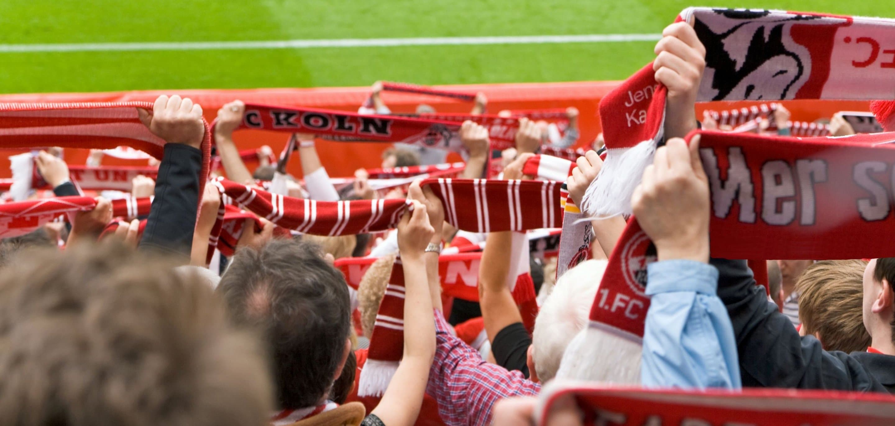 Fußballfans im Stadion halten Schals des 1. FC Köln hoch - Symbolbild für Hotspots von NetCologne im Stadion