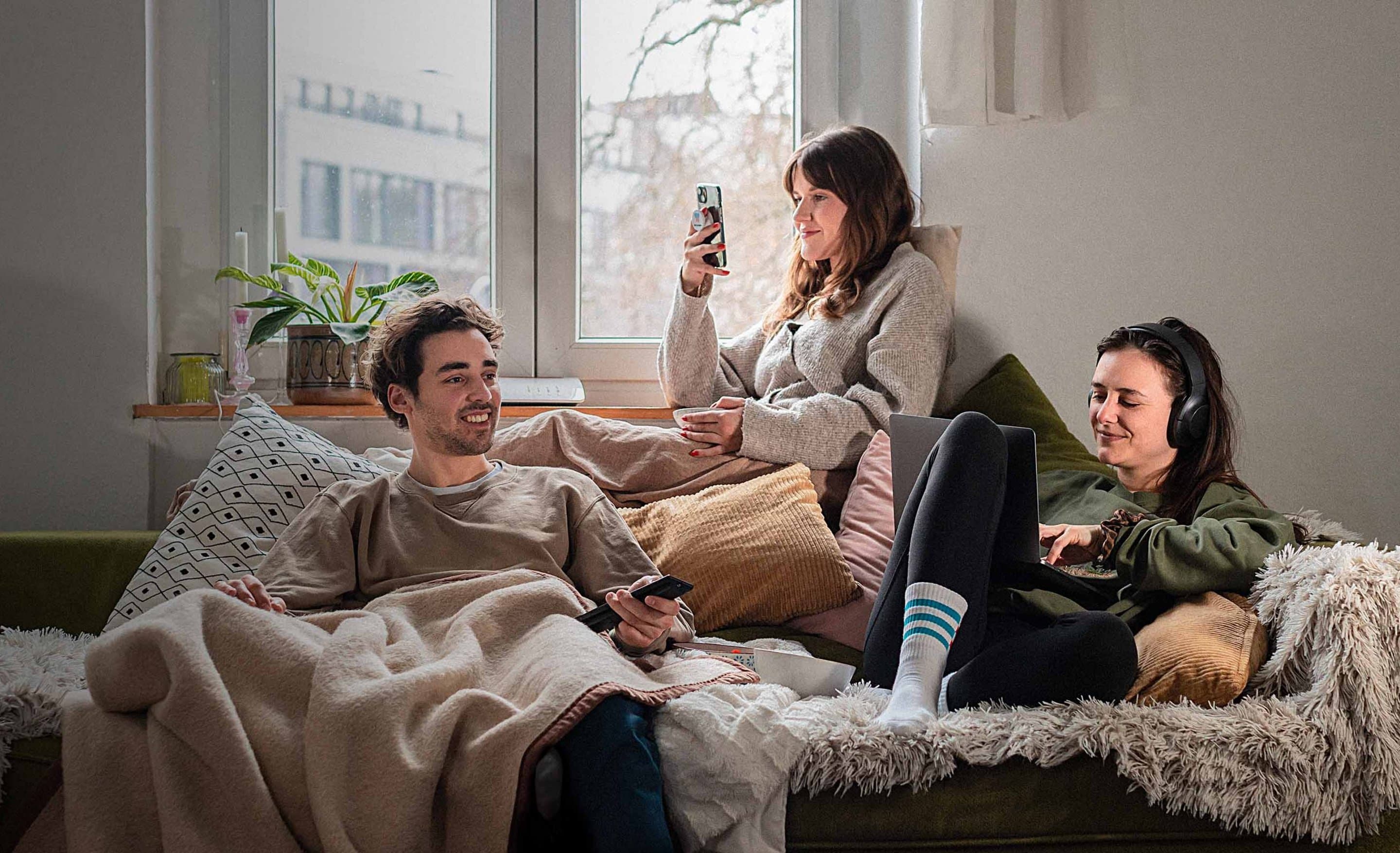DSL Tarife von NetCologne Eine Gruppe junger Leute sitzen gemeinsam auf der Couch und nutzen mobile Geräte.