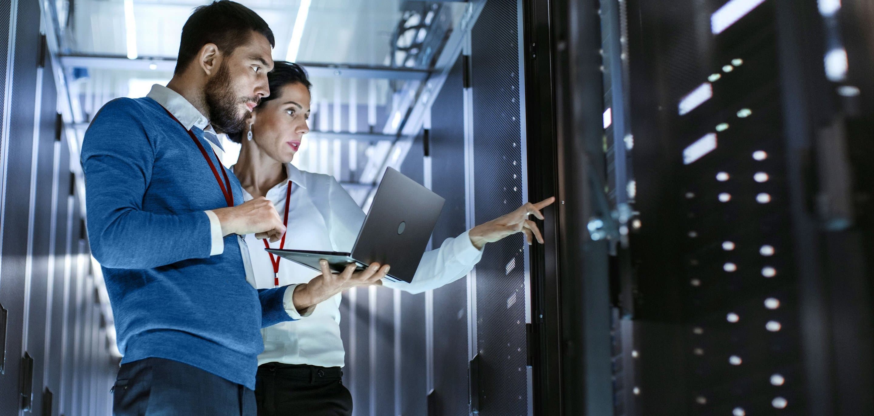 Serverraum Zwei Personen im Serverraum, eine mit Laptop, die andere zeigt auf ein Serverrack.