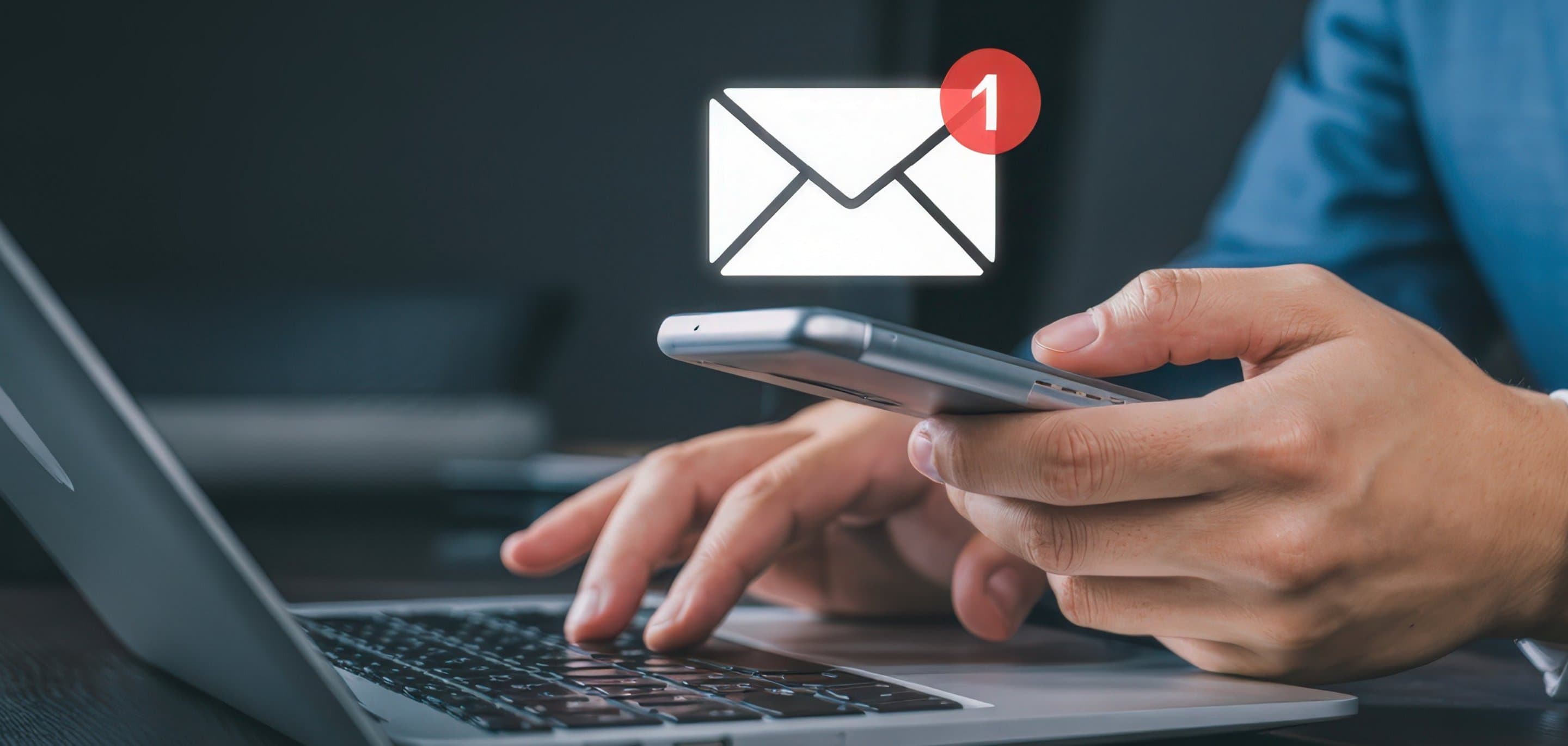 Person tippt am Laptop und hält Smartphone, darüber ein E-Mail-Symbol mit roter Benachrichtigung „1".