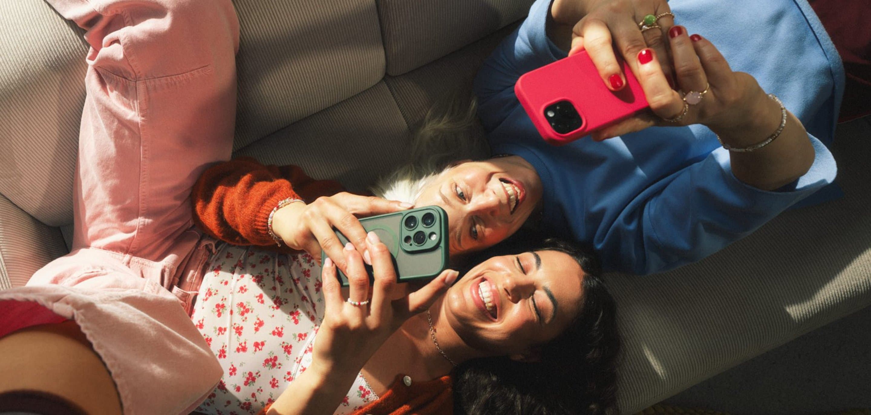 Zwei Personen liegen auf einem Sofa und halten jeweils ein Smartphone über sich, während sie gemeinsam auf die Displays schauen.