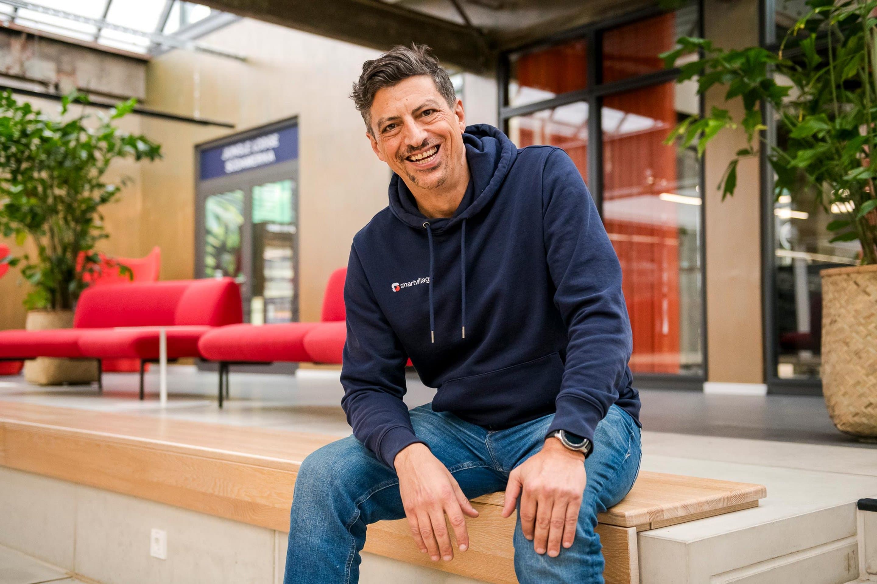 Gerd Krohn, CEO der smartvillage GmbH Ein Mann in einem blauen Hoodie sitzt auf einer Bank in einem Geschäftsgebäude