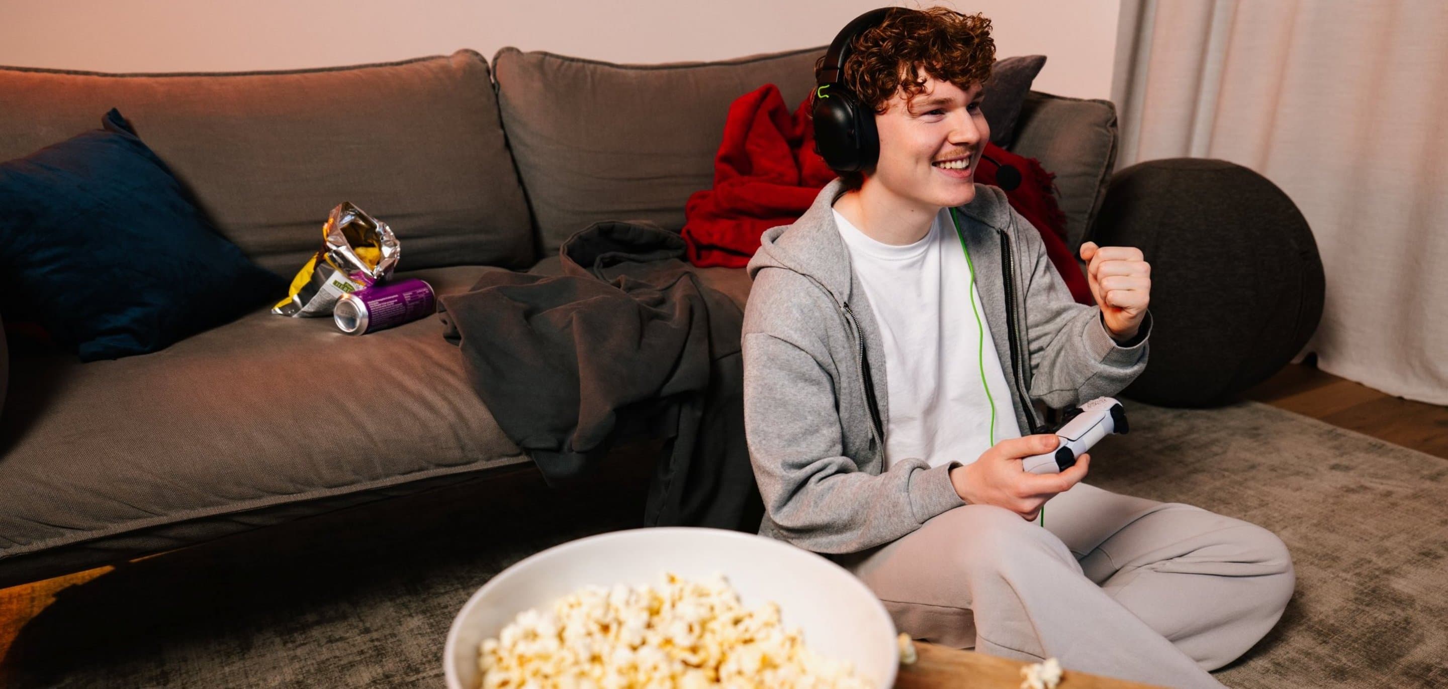 Person sitzt mit Headset und Controller beim Online-Gaming im Wohnzimmer.
