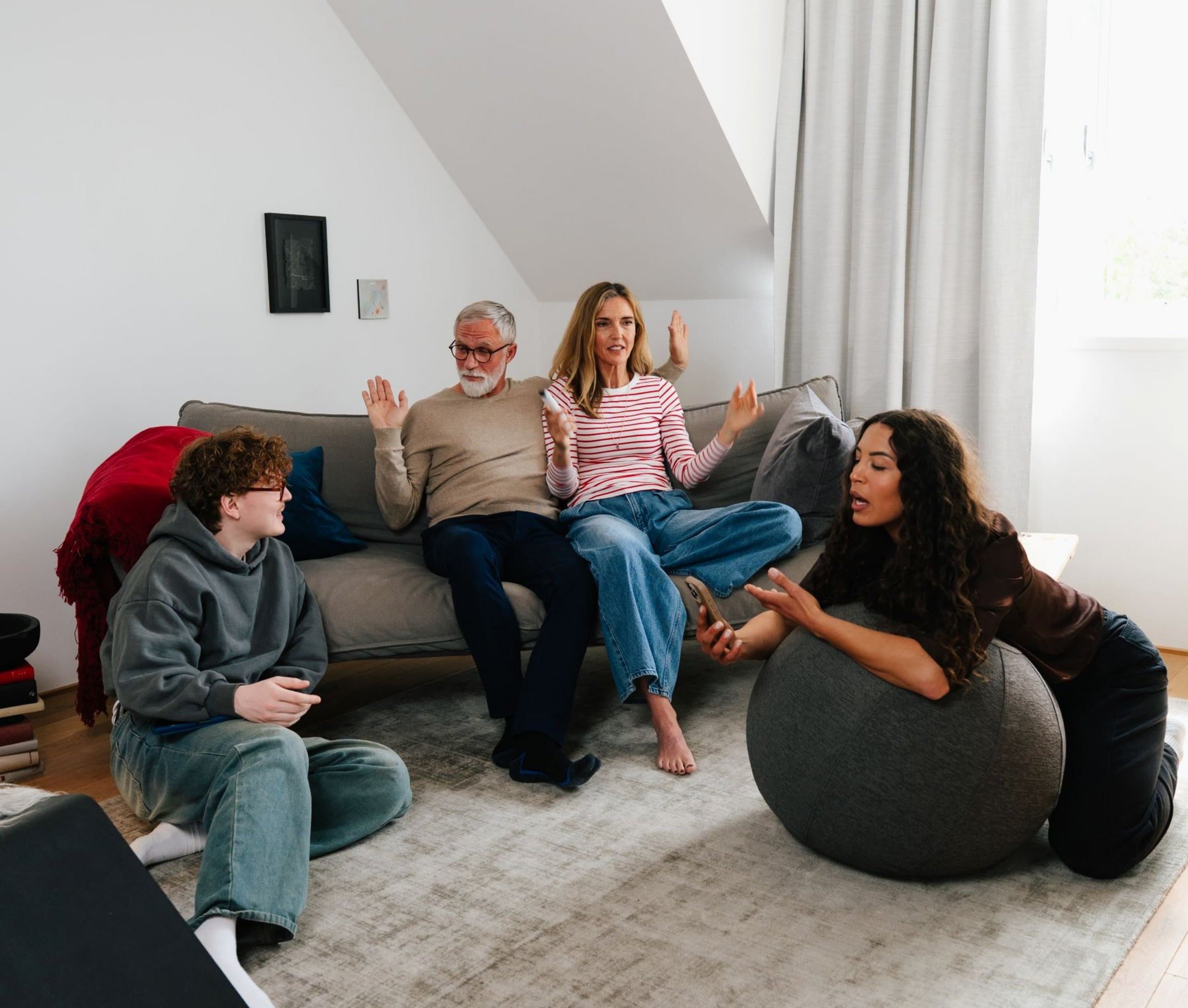 Vier Personen sitzen in einem Wohnzimmer und ärgern sich über die schlechte Internetverbindung an ihren jeweiligen Endgeräten - Symbolbild für zu geringe Bandbreite