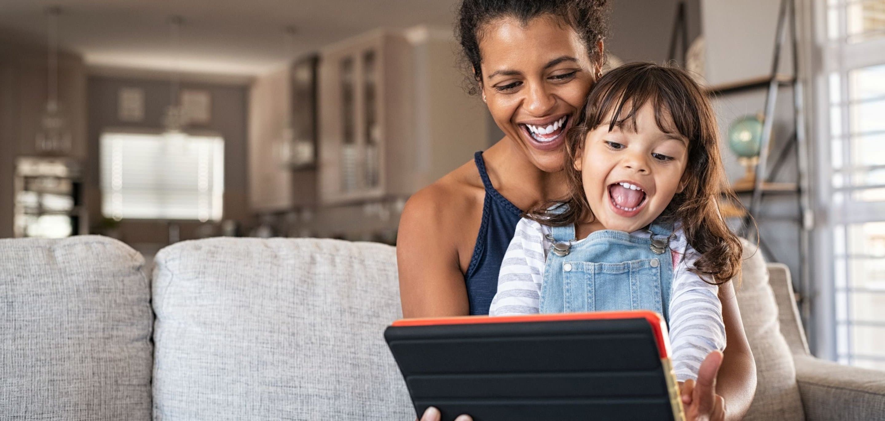 Digitales Leben: Erwachsene Person und Kind sitzen auf dem Sofa und schauen fröhlich auf ein Tablet – gutes Internet , Streaming und stabiles WLAN für die ganze Familie