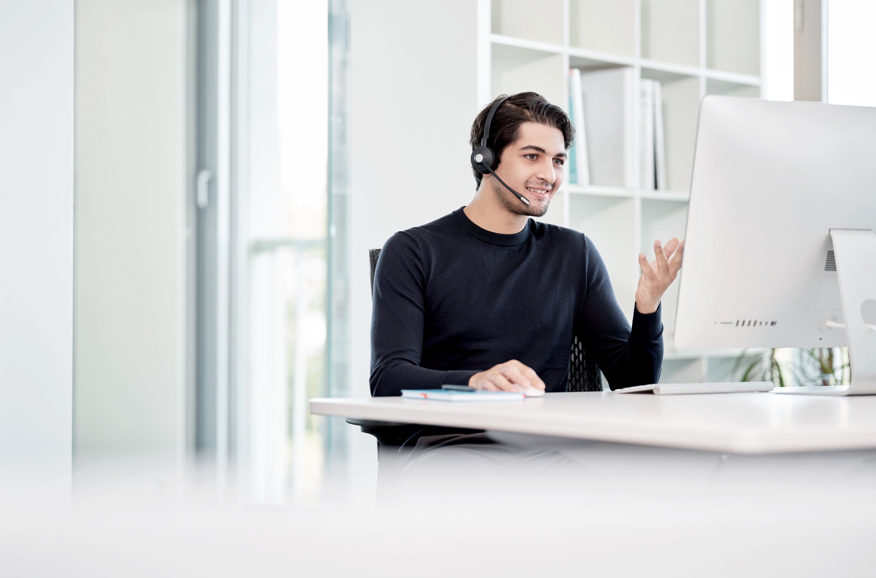Microsoft Teams Telefonie Mann mit Headset sitzt am Dektop und telefoniert