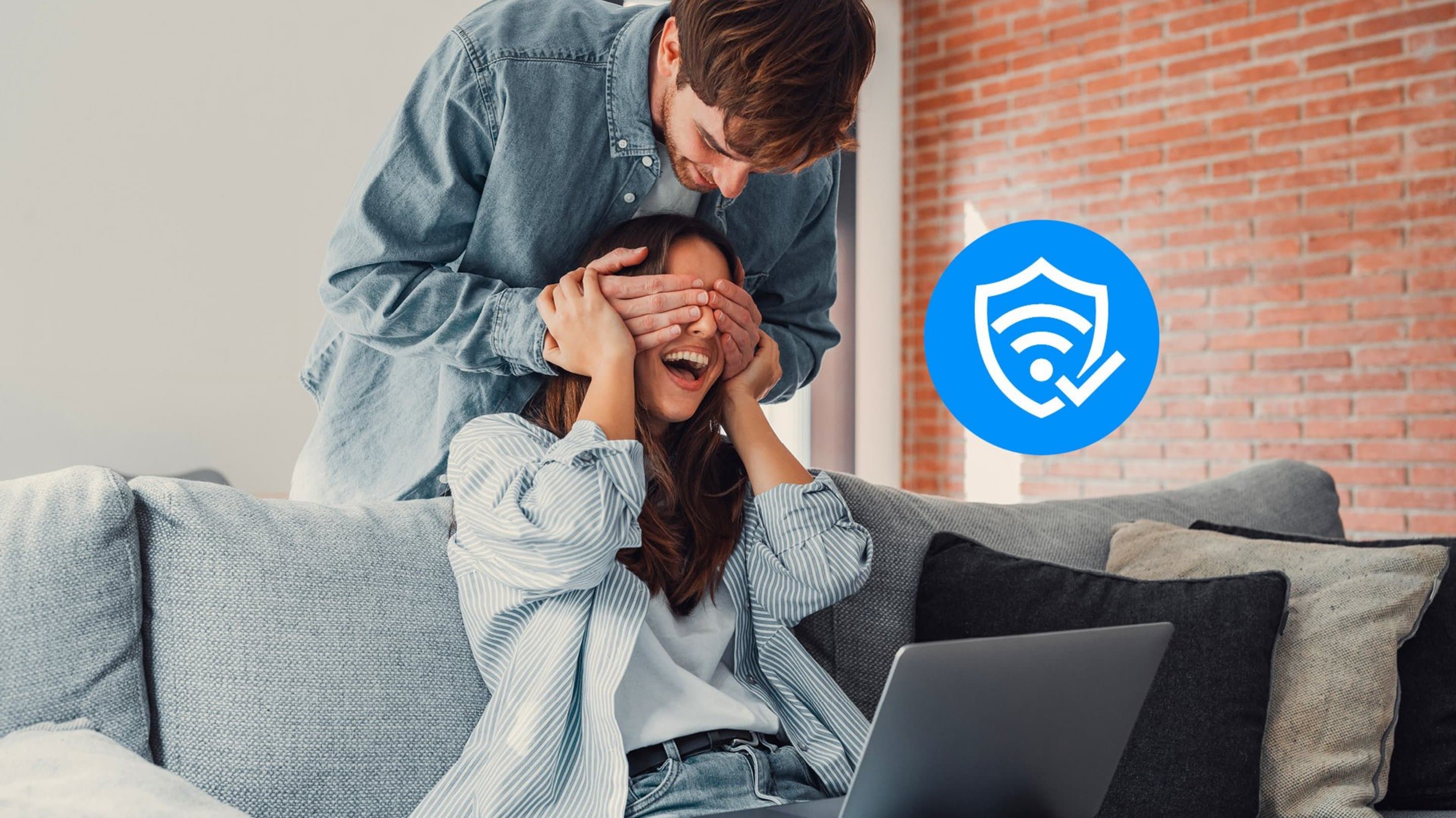 WLAN Service Plus Frau sitzt auf lachend auf Couch und bekommt Augen von Mann zugehalten, der hinter ihr steht