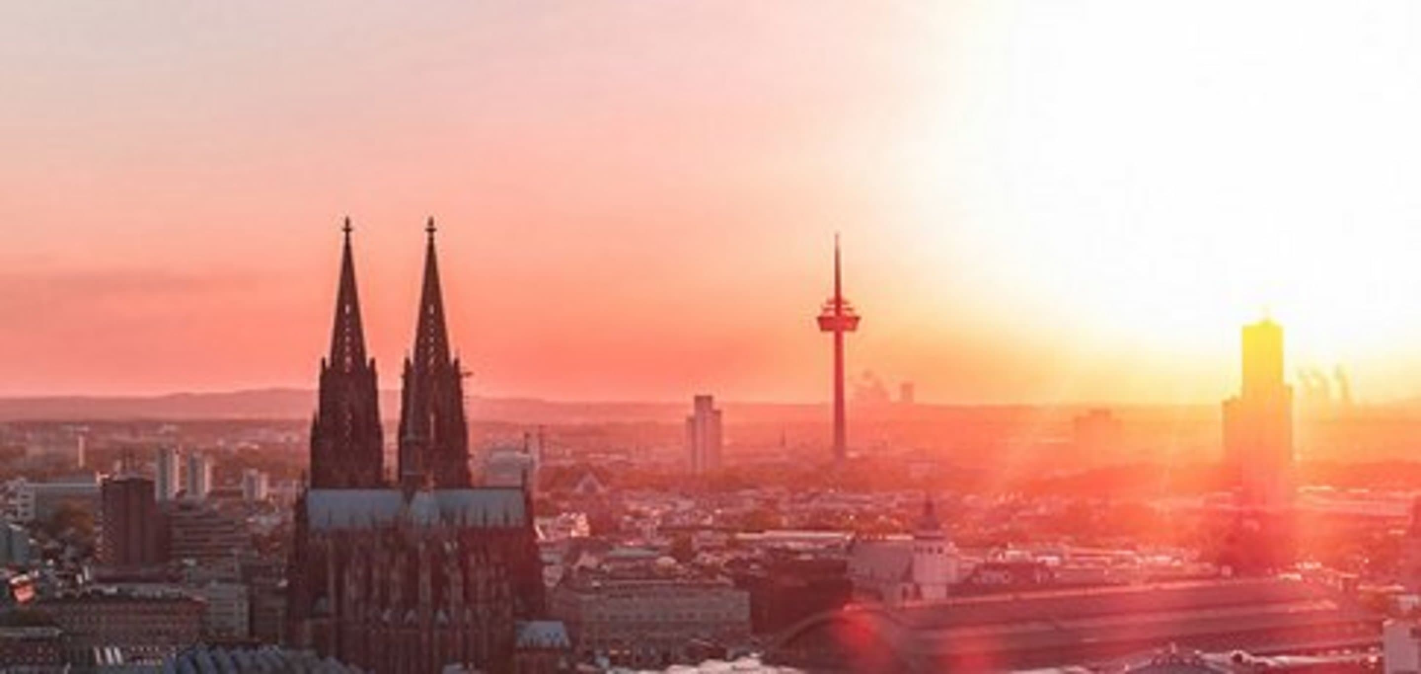 Skyline von Köln bei Sonnenuntergang mit den Türmen des Kölner Doms und dem Fernsehturm Colonius in warmem rot-orangefarbenem Licht