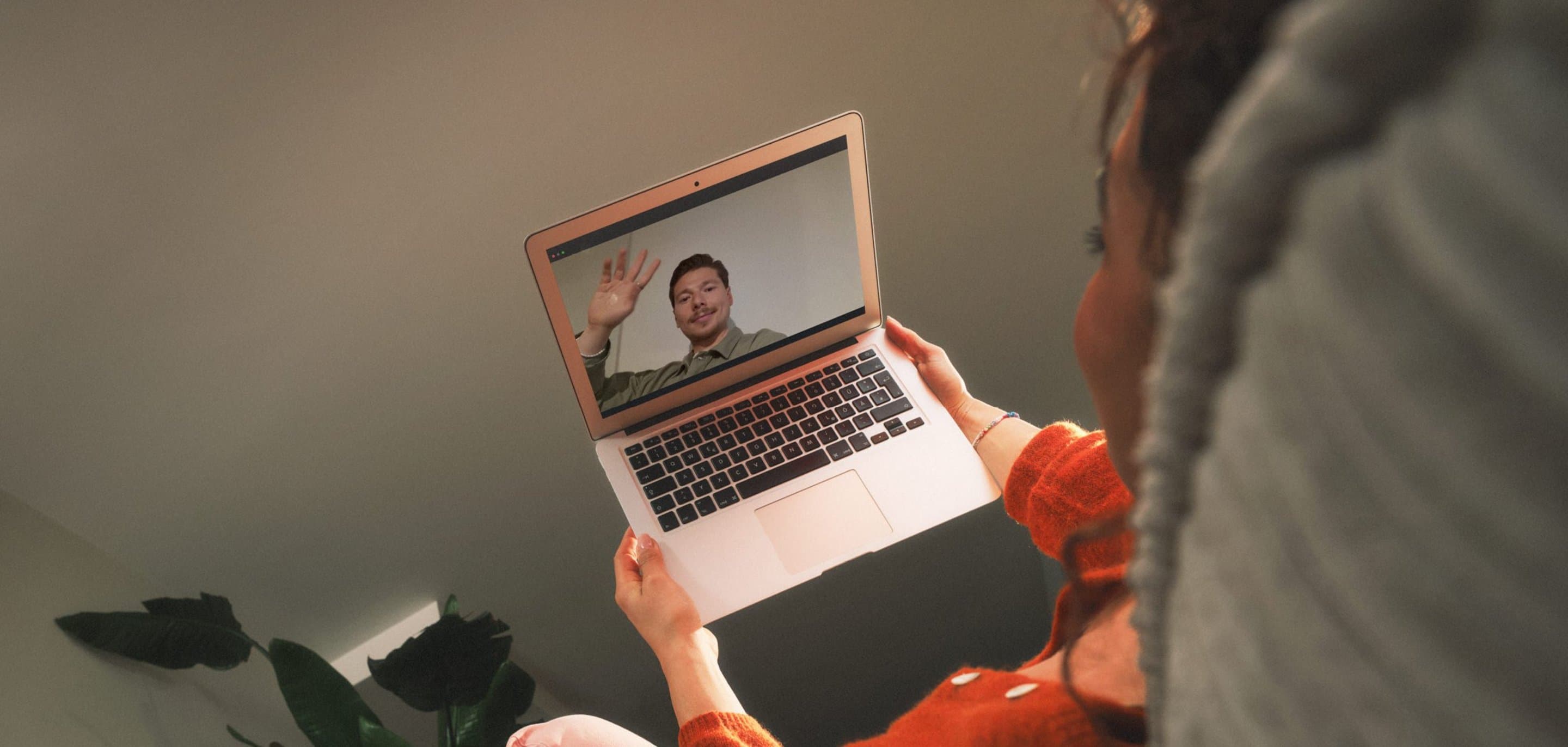Eine Person hält einen geöffneten Laptop und führt einen Videocall, bei dem auf dem Bildschirm eine weitere Person zu sehen ist.