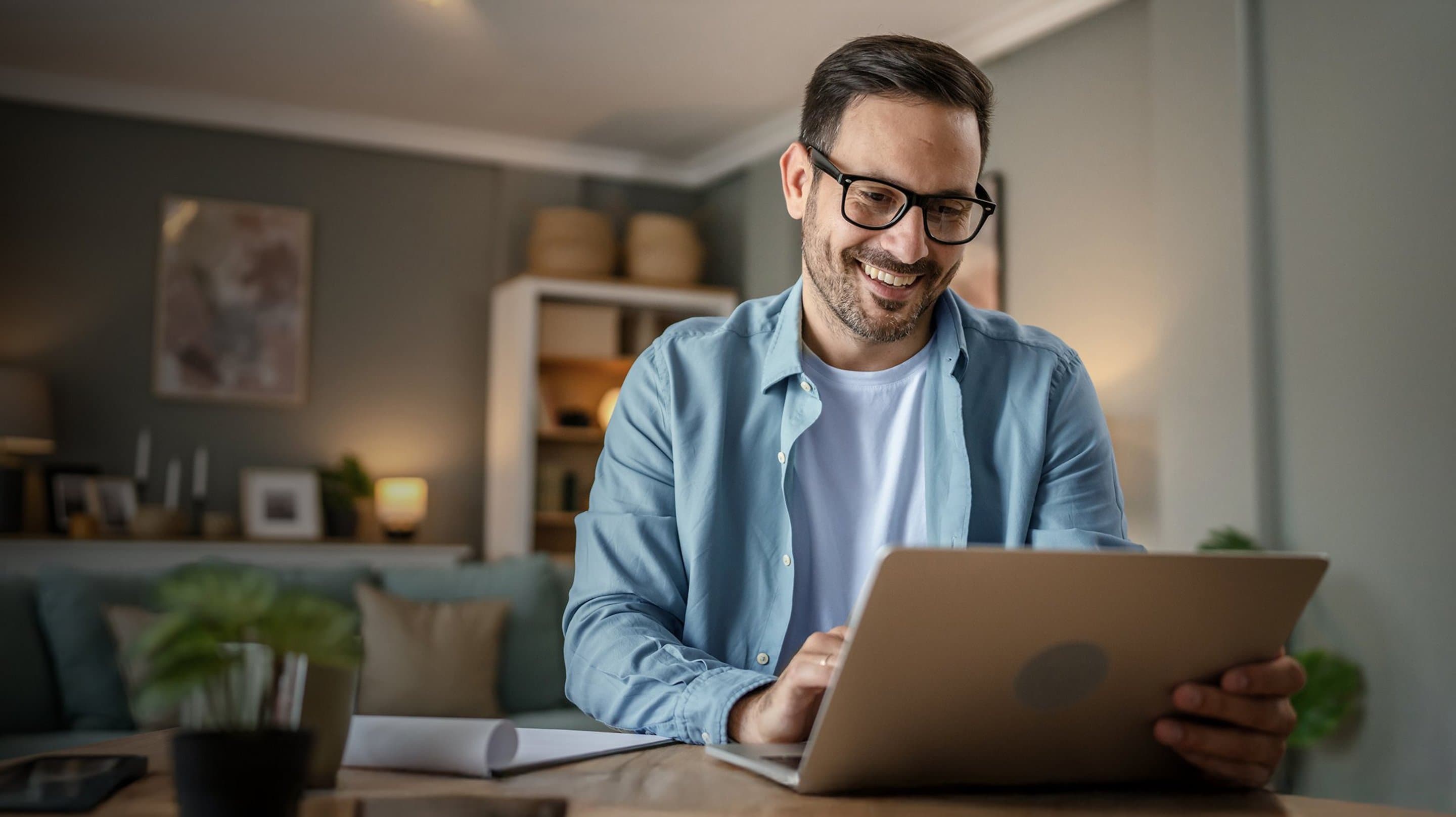 Mann sitzt am Tisch vor aufgeklapptem Laptop