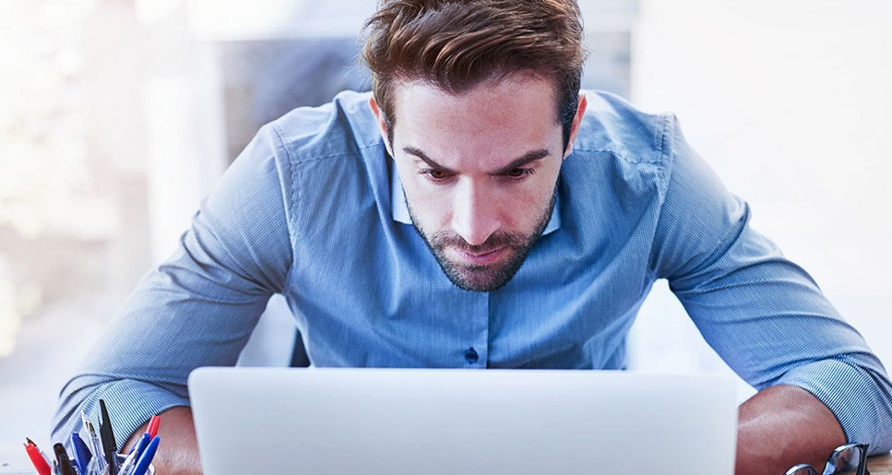 Mann sitzt vorgebeugt vor einem Laptop und schaut angestrengt auf diesen.