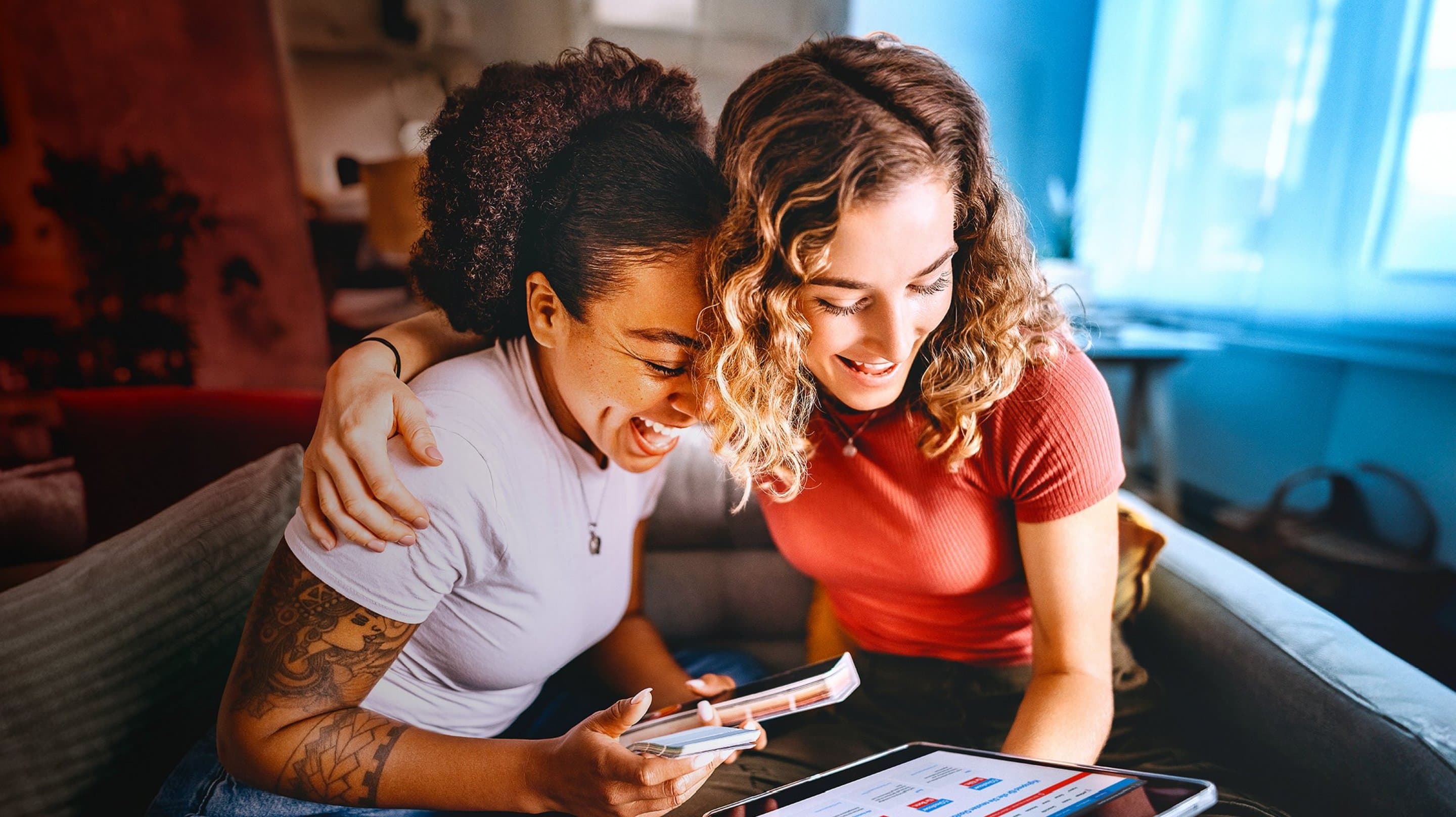 Zwei Frauen sitzen auf einem Sofa und schauen gemeinsam auf ein Tablet.