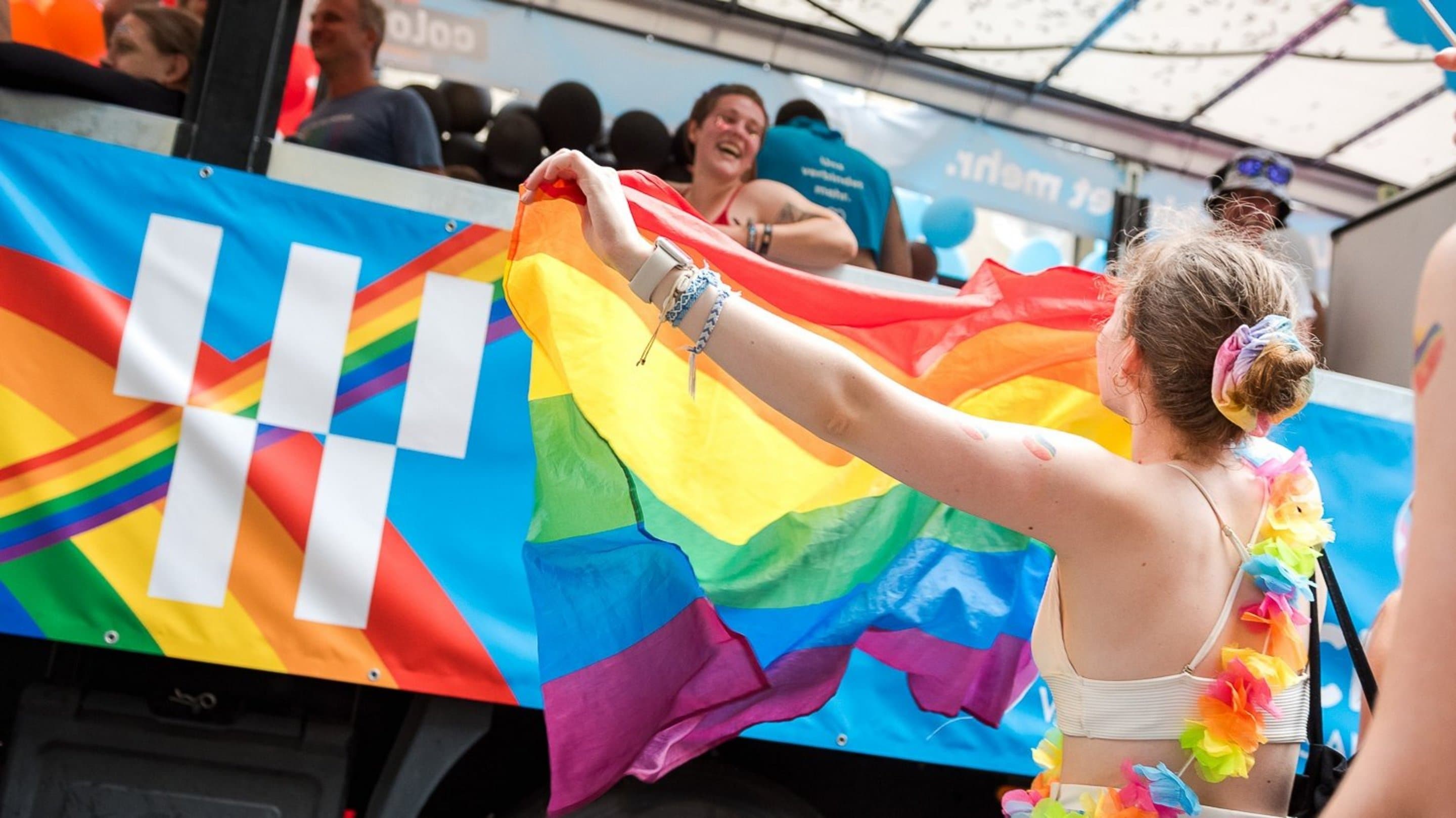 NetColgne_Pride Person mit Regenbogenflagge steht vor NetCologne Festwagen auf Christopher Street Day