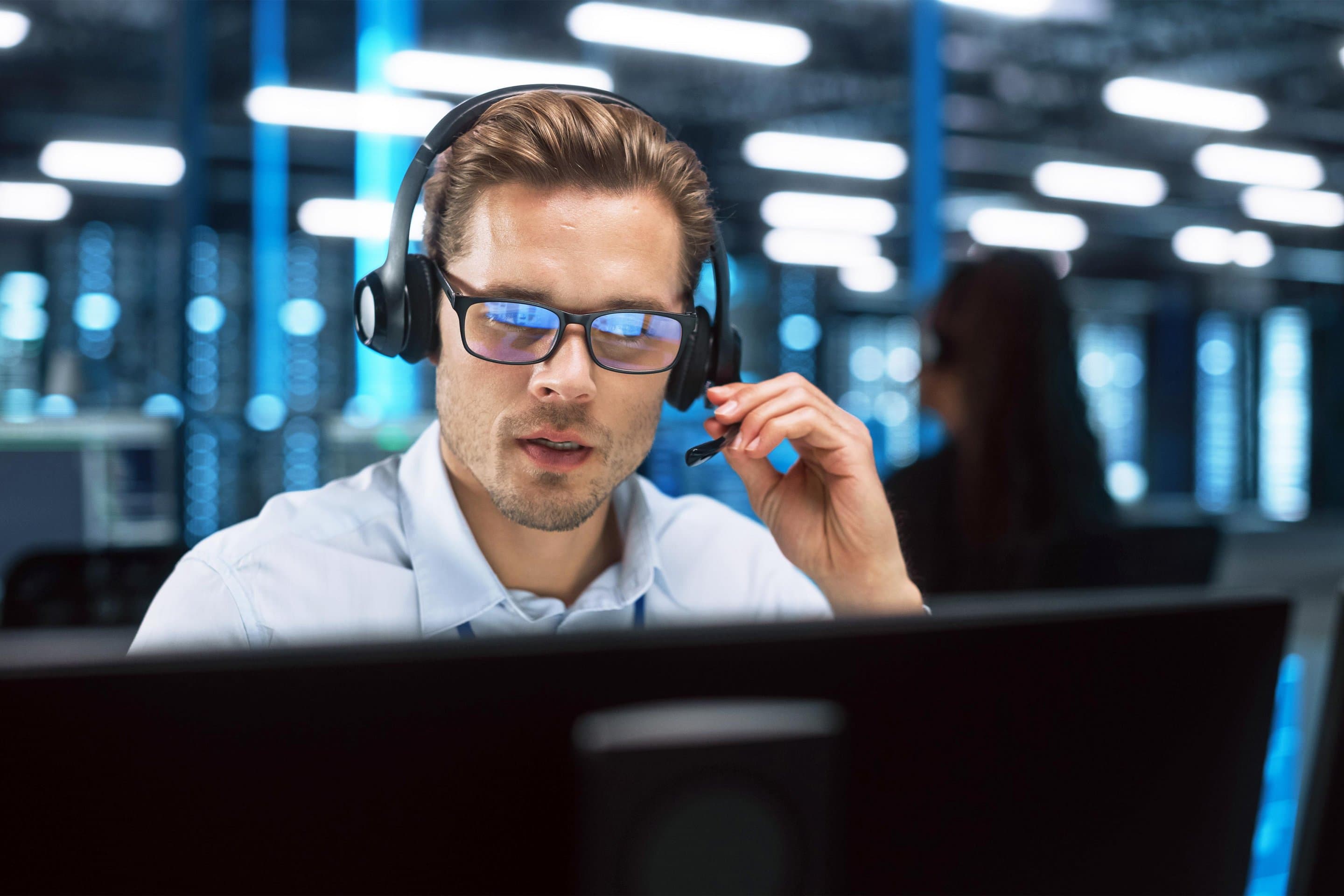 Symbolbild für Beratung und Bestellung Mann mit Brille und Headset sitzt am Desktoprechner.
