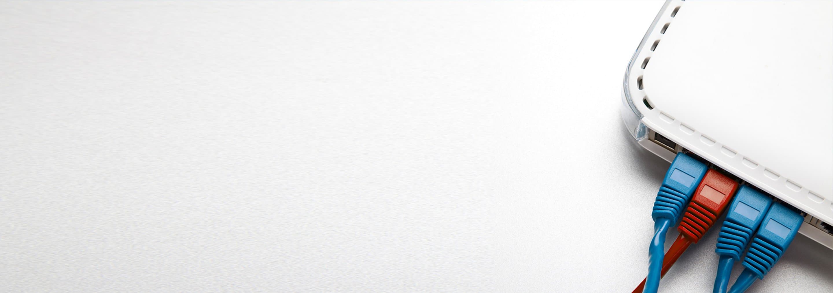 Grauer Hintergrund auf dem in der Ecke ein Teil eines Routers zu sehen ist, in dem blaue und rote Kabel stecken.